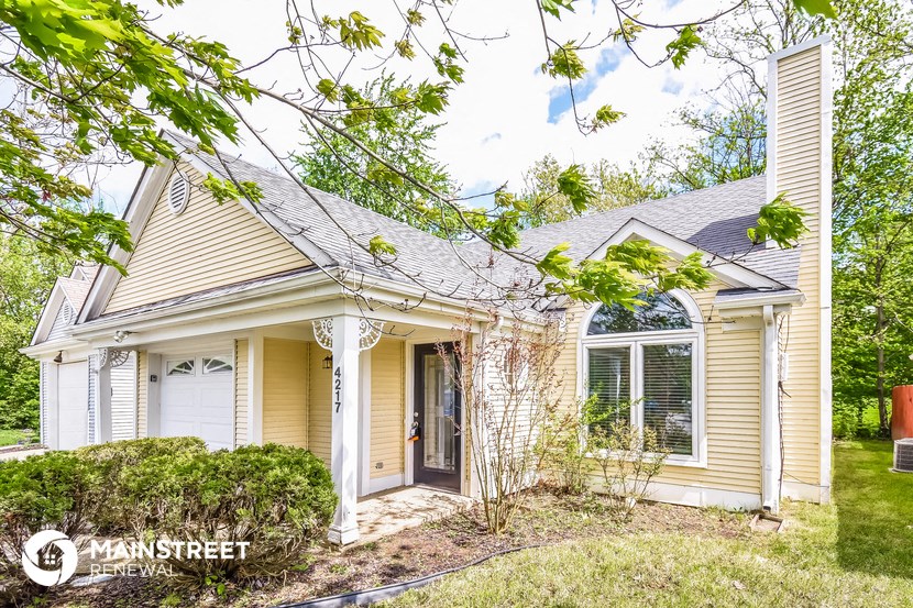 the front of a yellow house with white shutters and a lawn and trees
