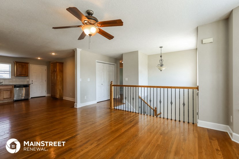 an empty living room with a ceiling fan and a staircase