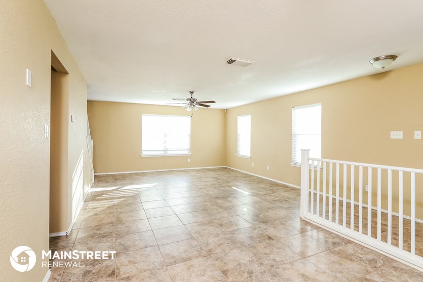 an empty living room with a white staircase and a ceiling fan