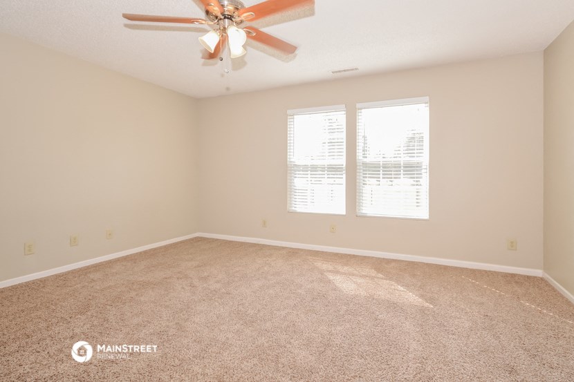 an empty living room with a ceiling fan and two windows