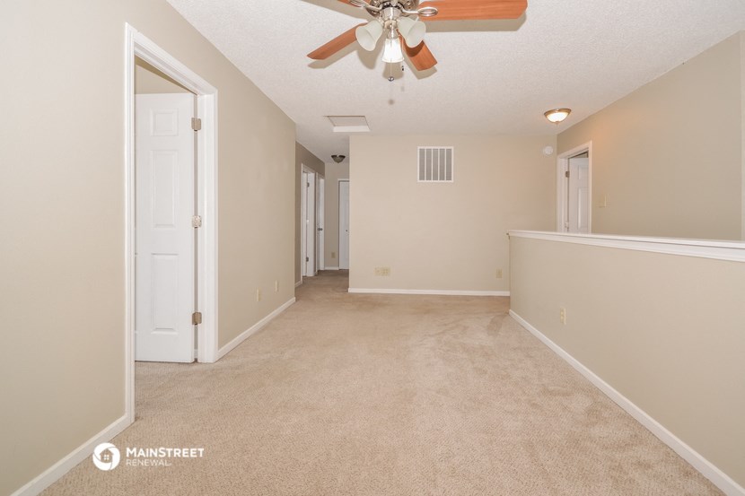 a spacious living room with carpet and a ceiling fan