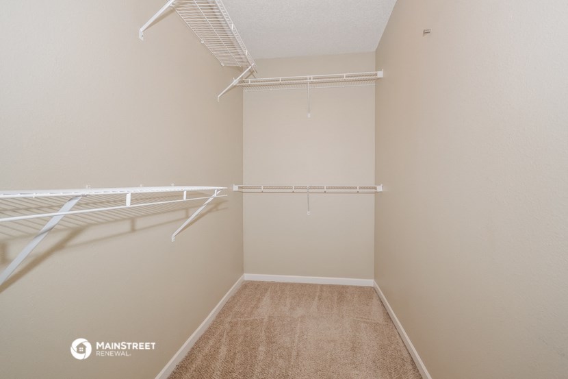 a spacious walk in closet with a mirrored wall and a white closet with white shelves