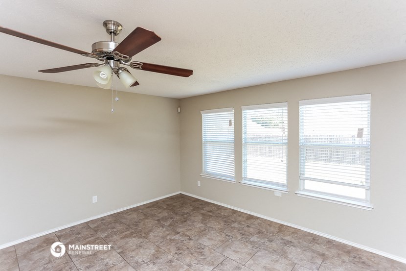 an empty living room with a ceiling fan and three windows