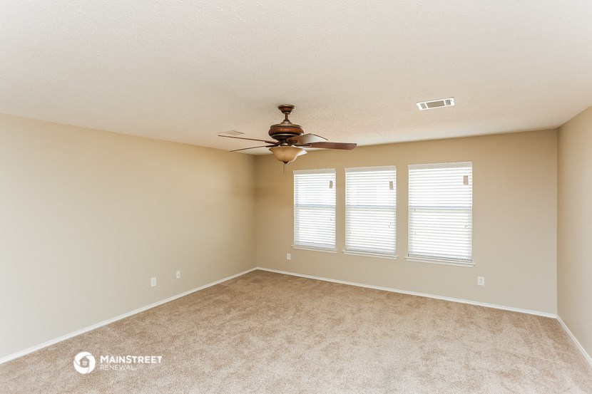 an empty living room with a ceiling fan and two windows