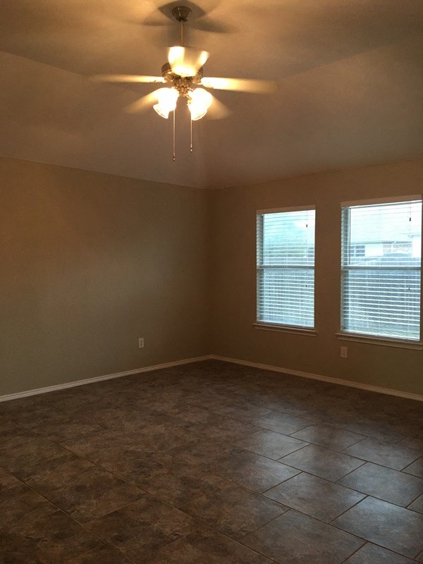 an empty living room with a ceiling fan and two windows