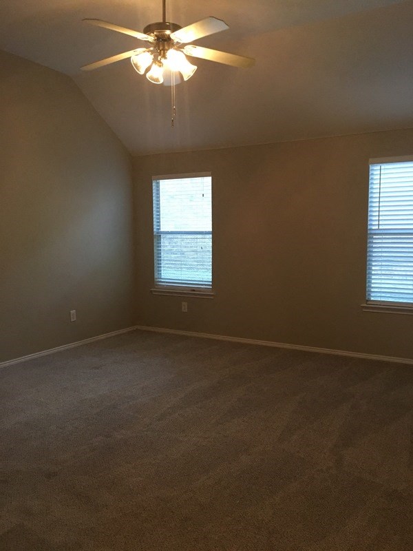an empty room with a ceiling fan and two windows