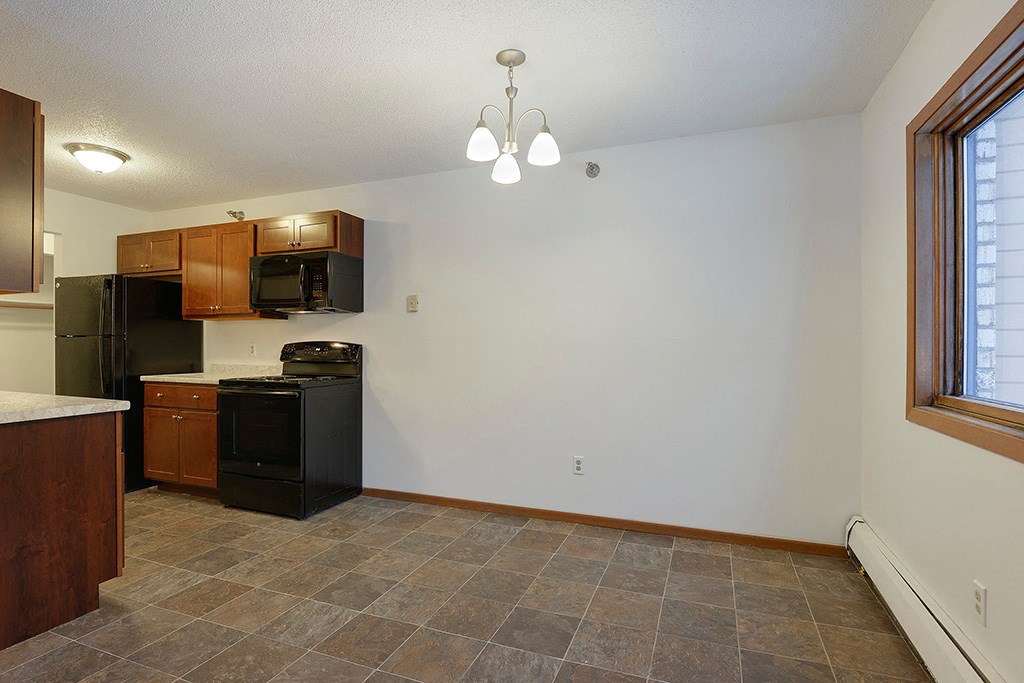 an empty kitchen with a black refrigerator and a window