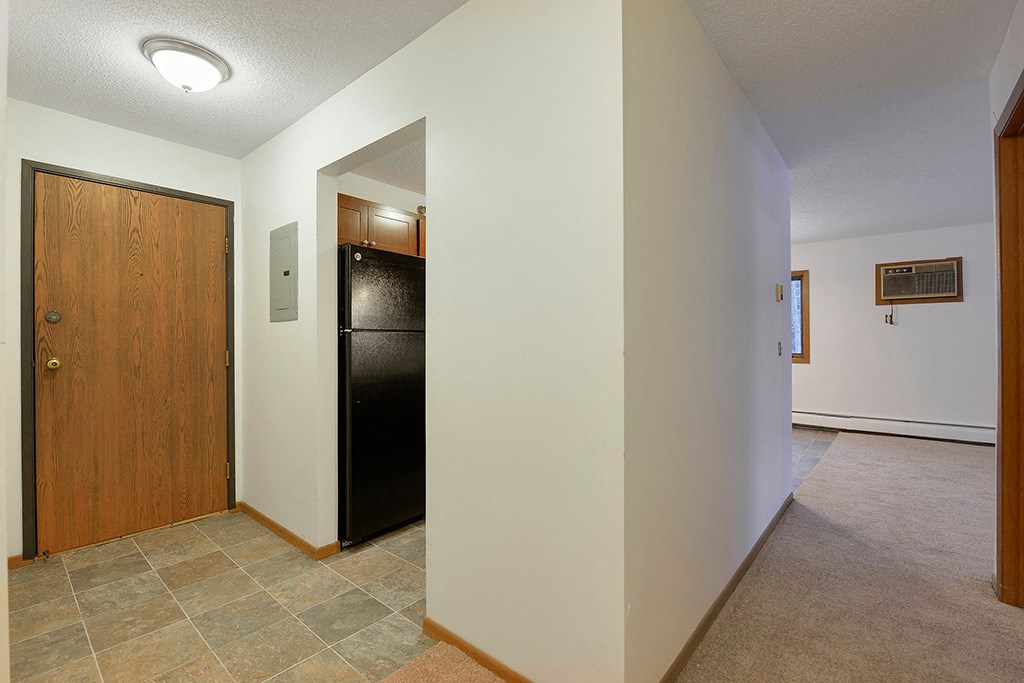 a hallway with a black refrigerator and a wooden door