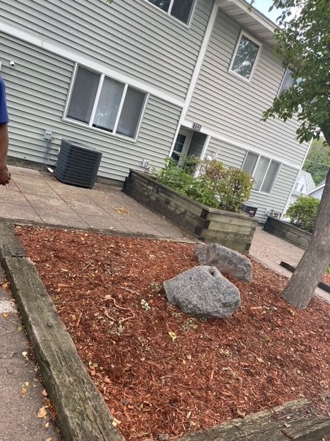 a yard with a rock and mulch in front of a house