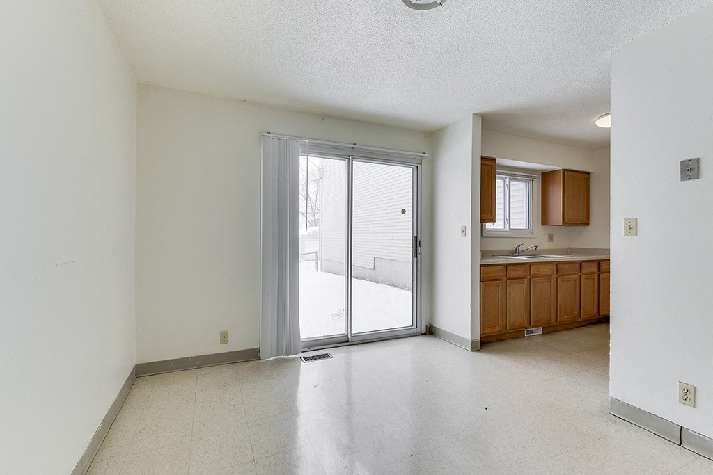 an empty living room with a sliding glass door to a kitchen