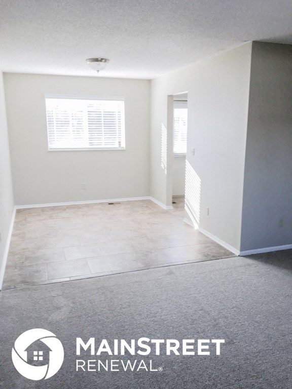 an empty living room with gray carpet and white walls and a window