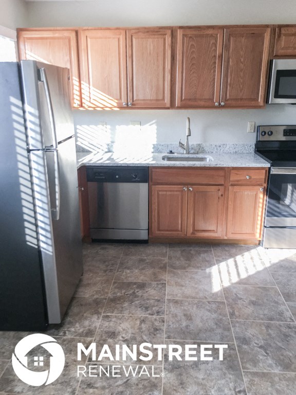 an empty kitchen with wooden cabinets and a stainless steel refrigerator