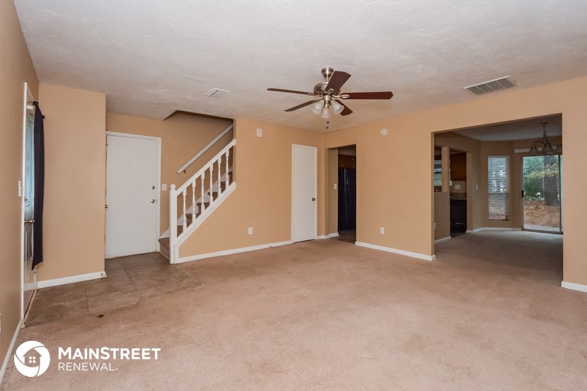 an empty living room with a ceiling fan and a staircase