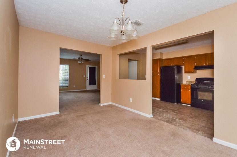 an empty living room with a kitchen in the background