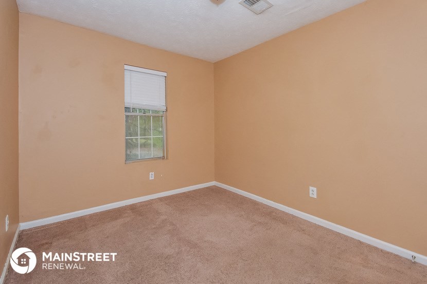 the bedroom of a house with carpet and a window