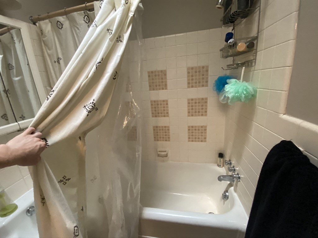 a person holding a shower curtain in a bathroom