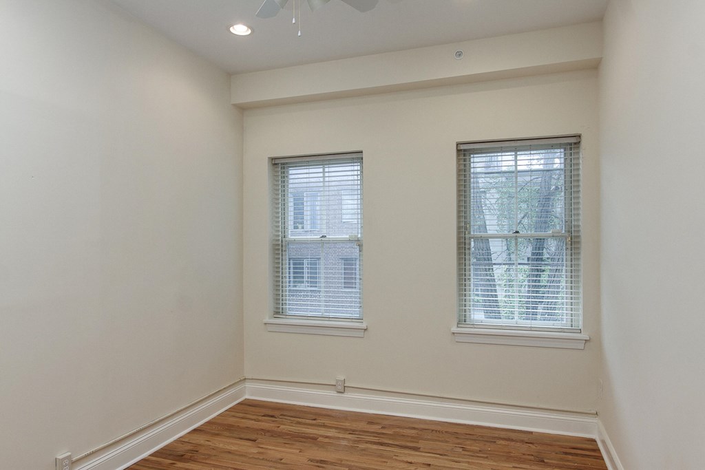 an empty room with two windows and a wooden floor