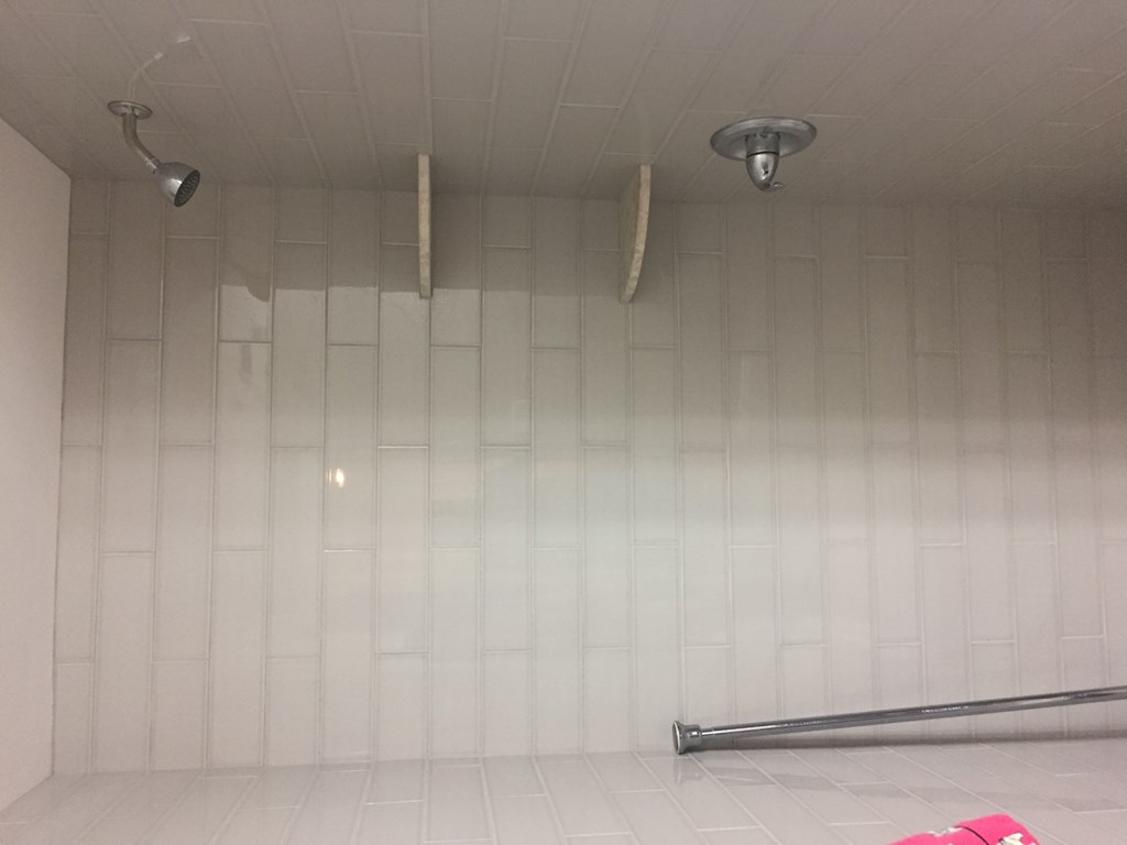 a large shower in a white tiled room with two showerheads on the ceiling