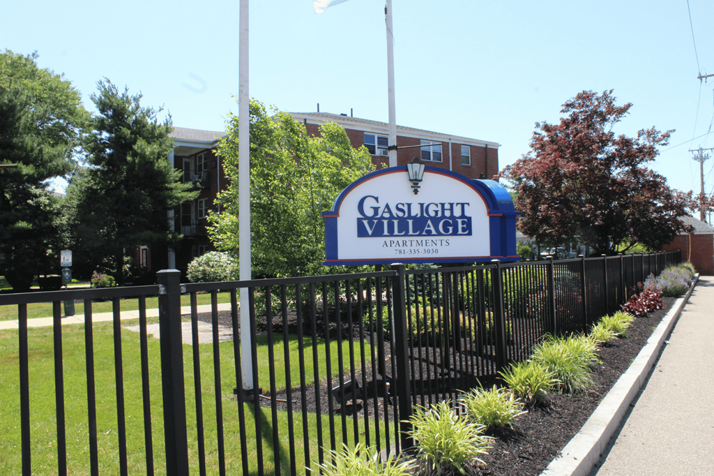 A sign for Gaslight Village Apartments is shown in front of a black fence.