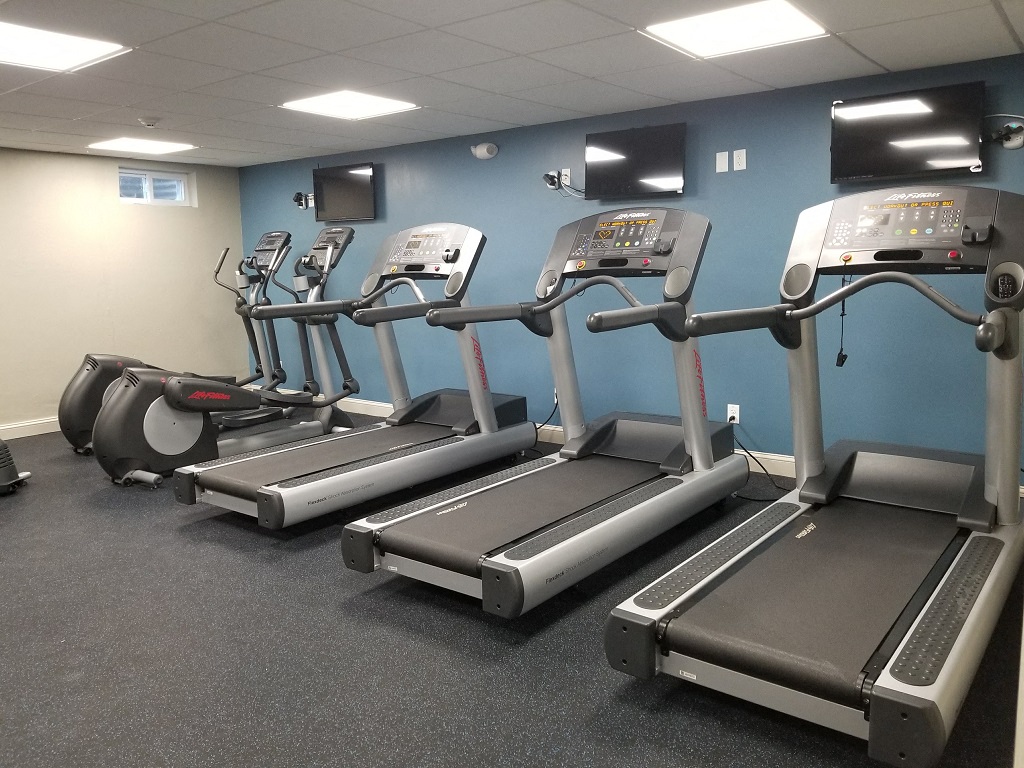a gym with four treadmills and monitors on the wall