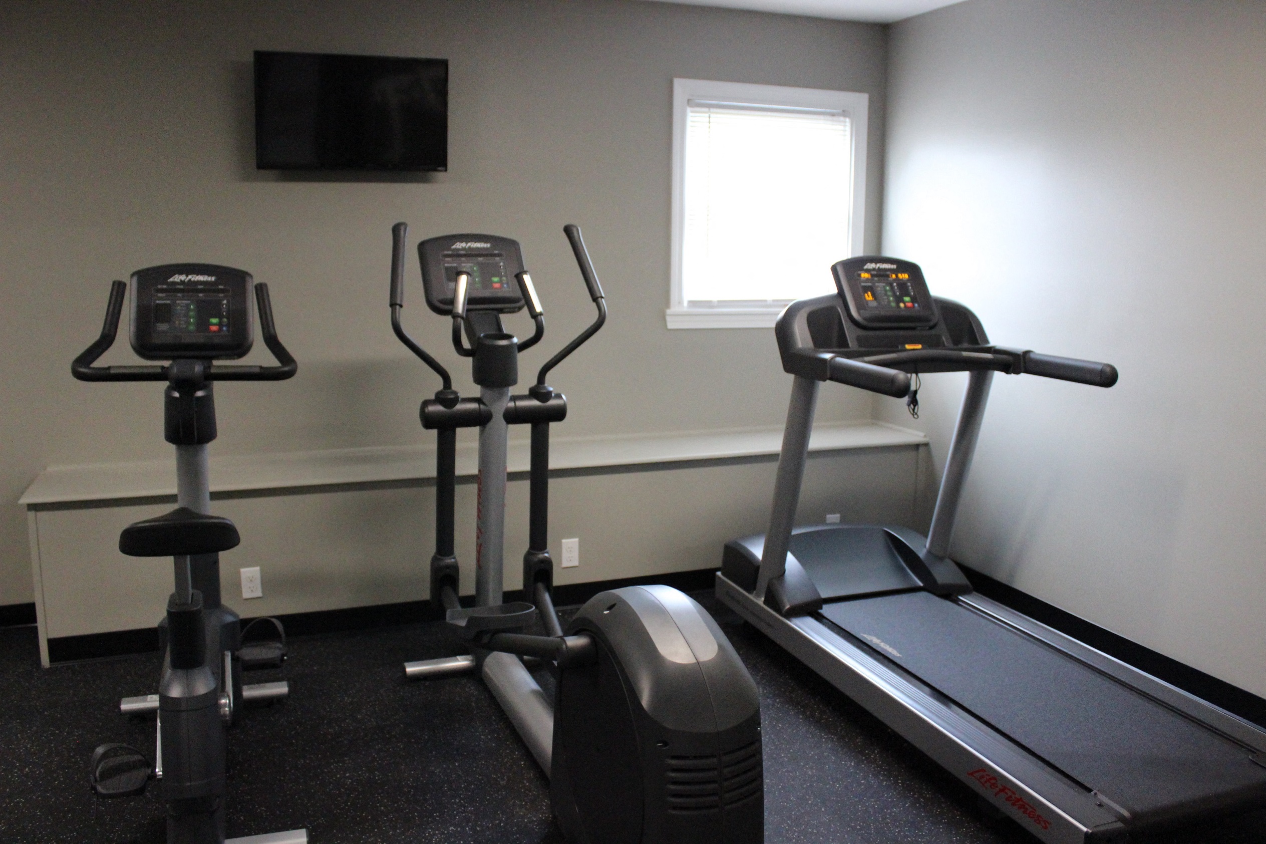 a gym with three exercise machines in a room with a window
