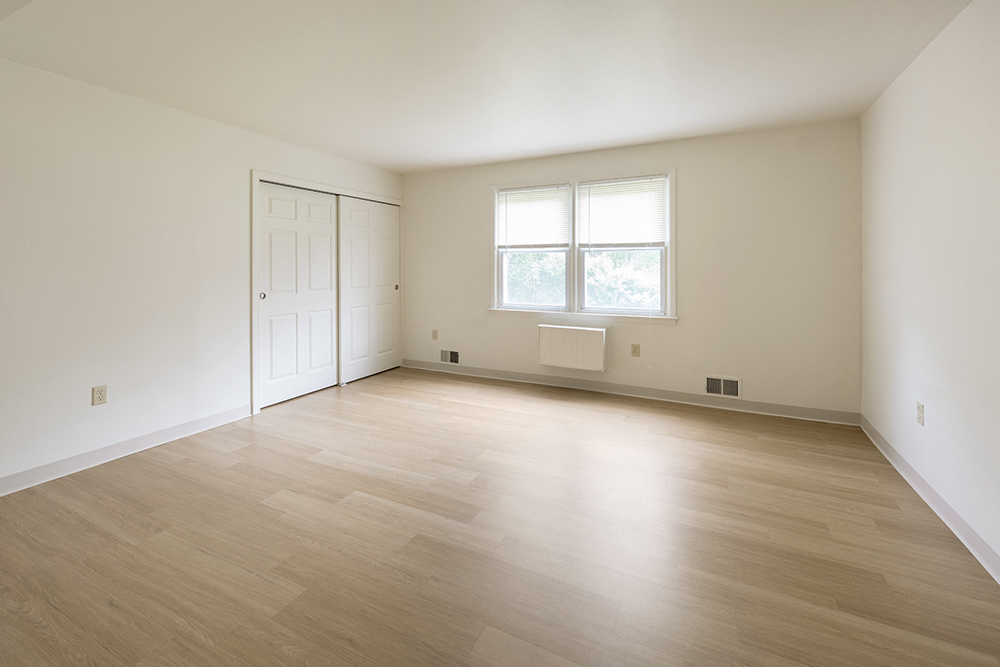 an empty living room with white walls and a window and wooden floors