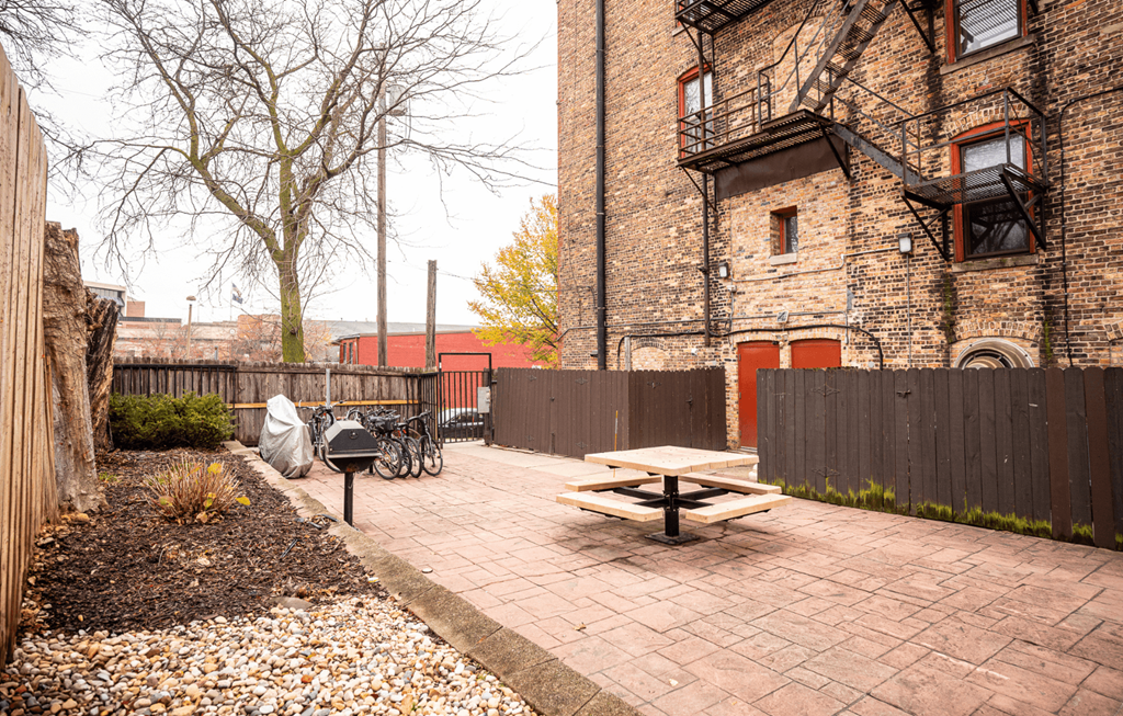 A brick patio with a picnic table and a bicycle in front of a brick building.