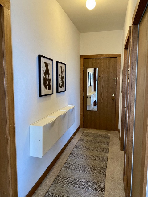 a hallway with a white wall with a shelf and a door