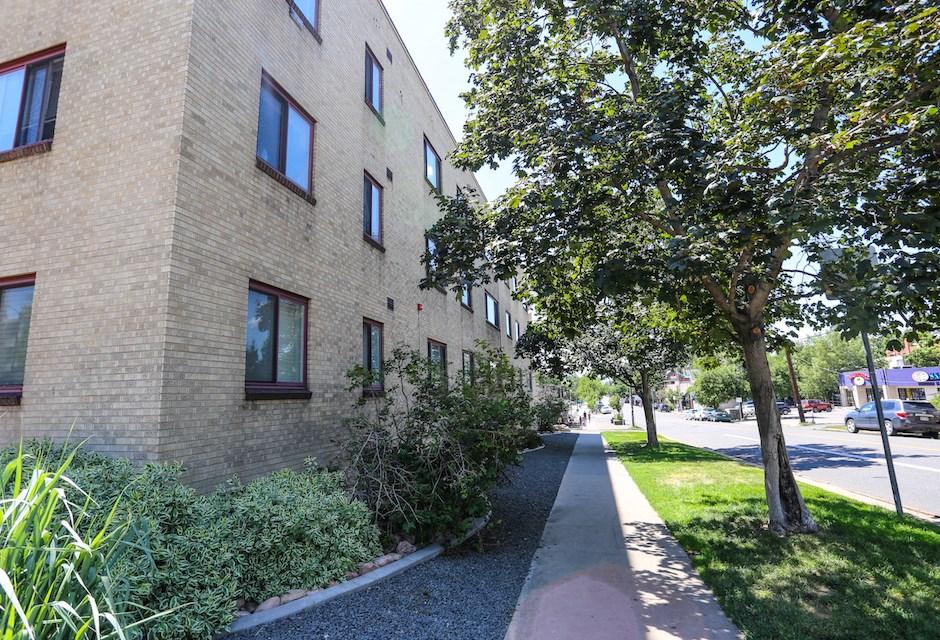 the side of a brick building with a sidewalk and trees