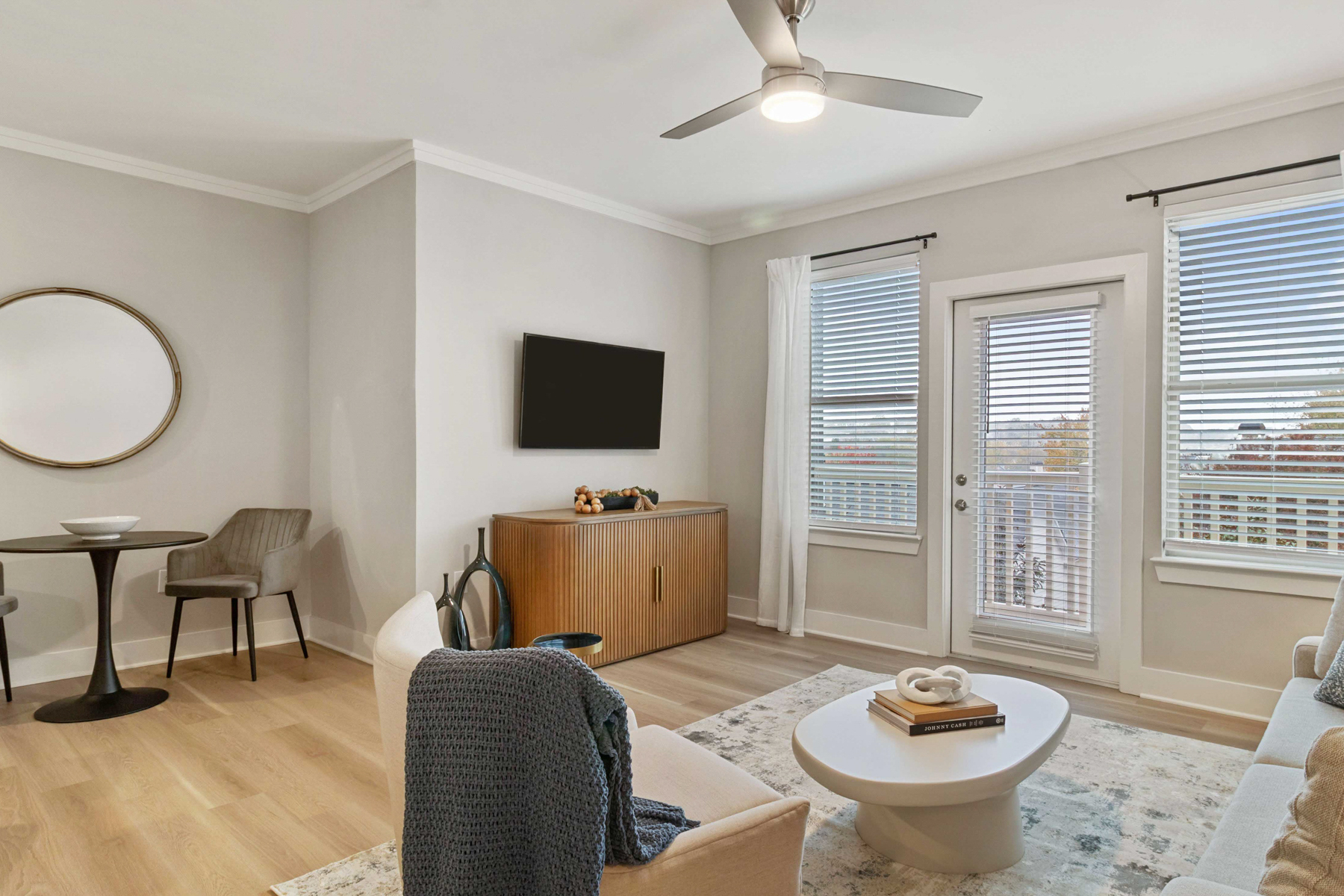 A living room with a grey chair and a round mirror on the wall.