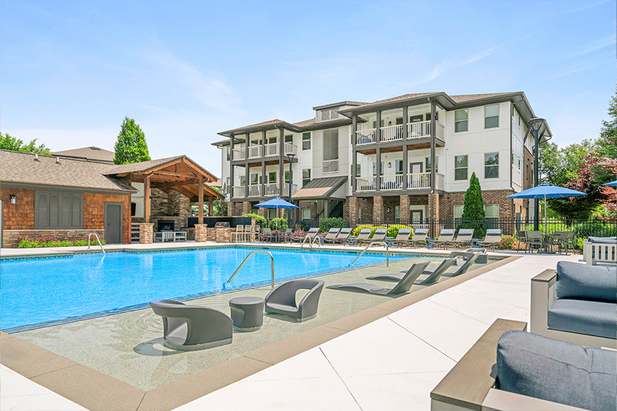 A large swimming pool with lounge chairs and umbrellas in front of a multi-story apartment building.