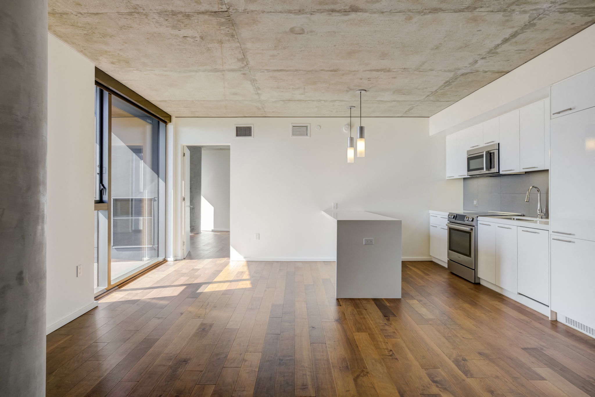 an empty living room with a kitchen and a glass door