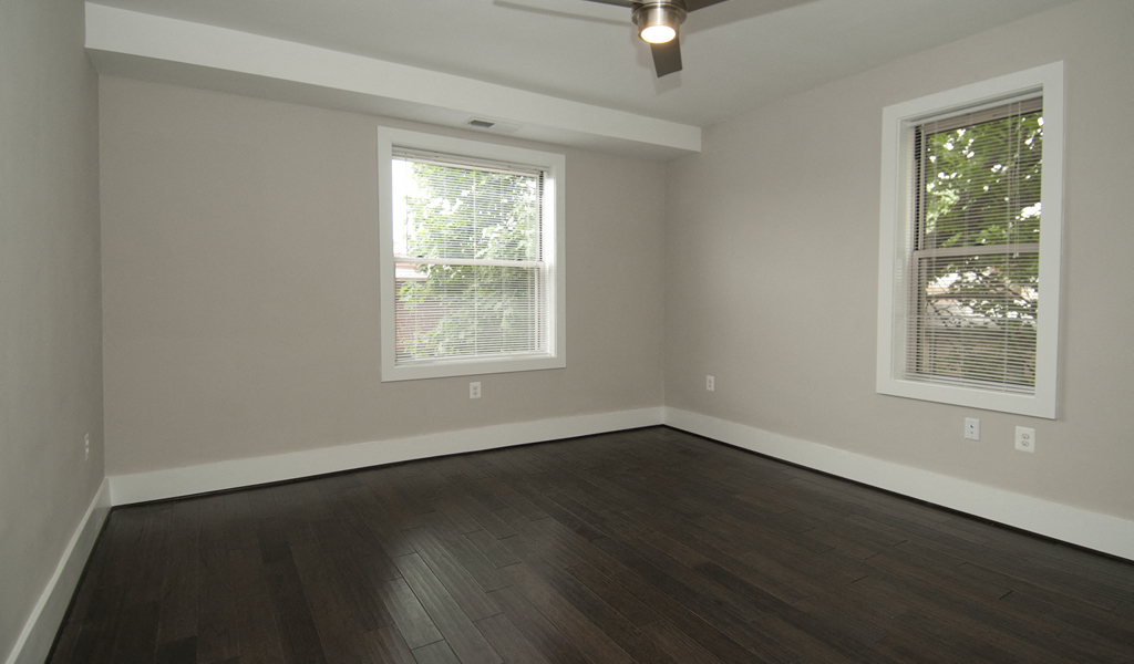 an empty living room with wood floors and two windows