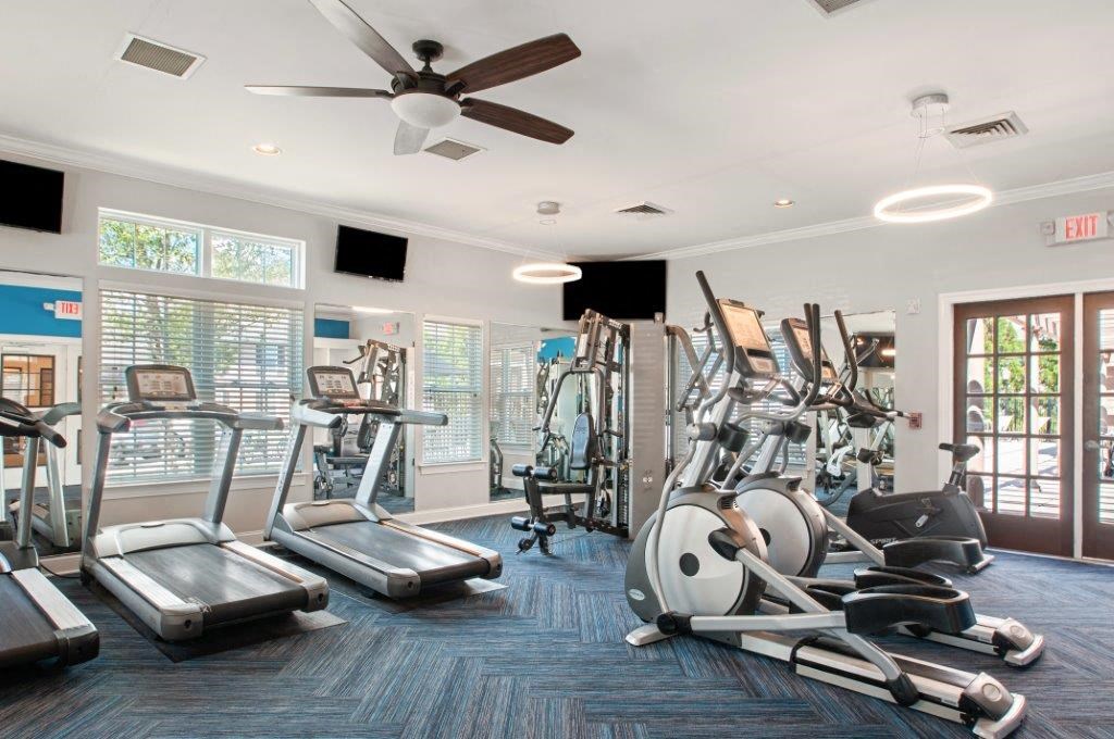 a gym with cardio machines and a ceiling fan