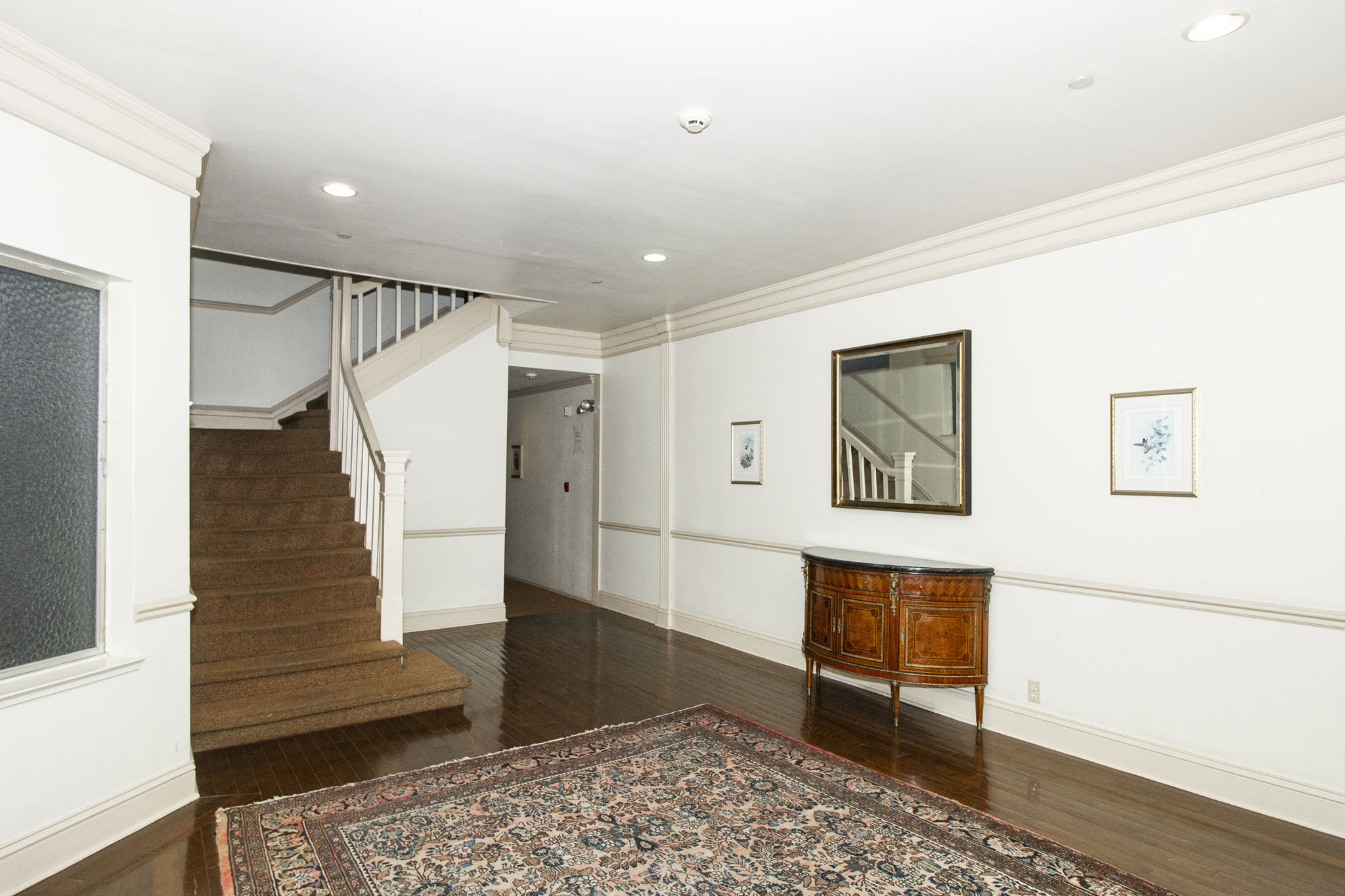 A hallway with a rug on the floor and a wooden cabinet.