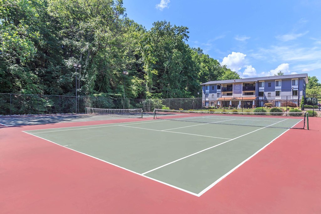 a tennis court with a building and trees in the background