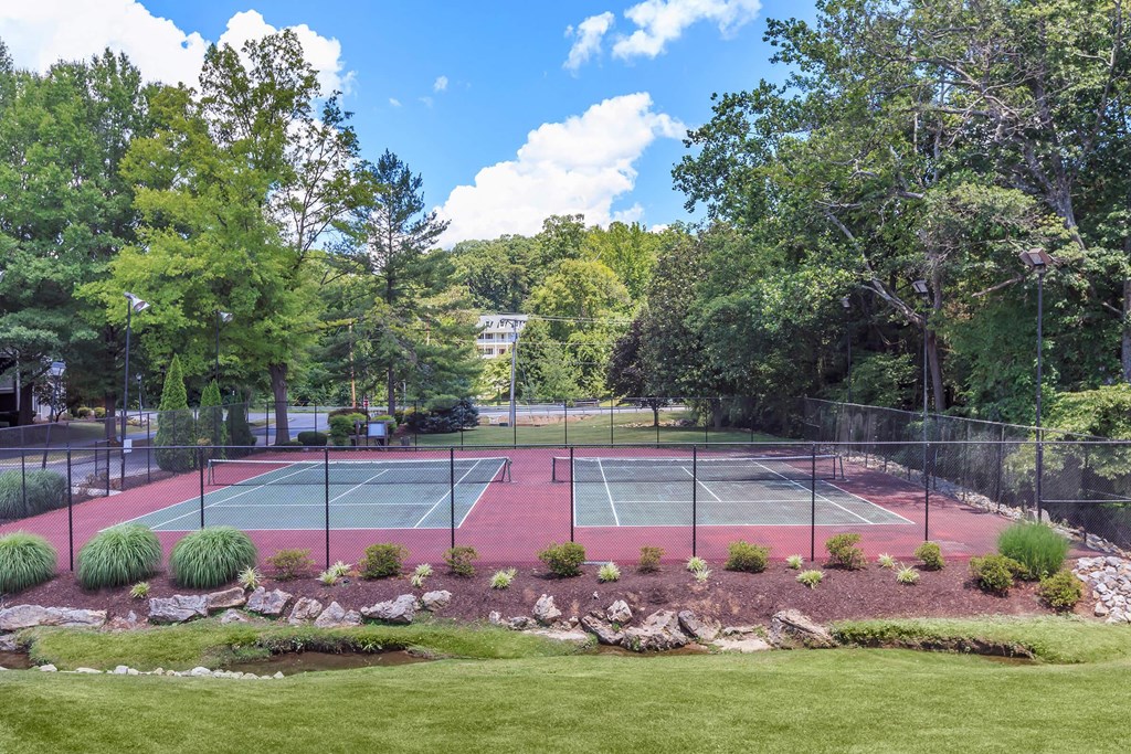 a tennis court with two tennis courts in front of trees