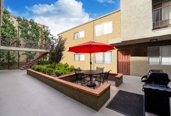 The courtyard at the Ridgeview apartment in Northridge with BBQ machine, patio seating, and an elevated planter with beautifully manicured plants. - Photo Gallery 2
