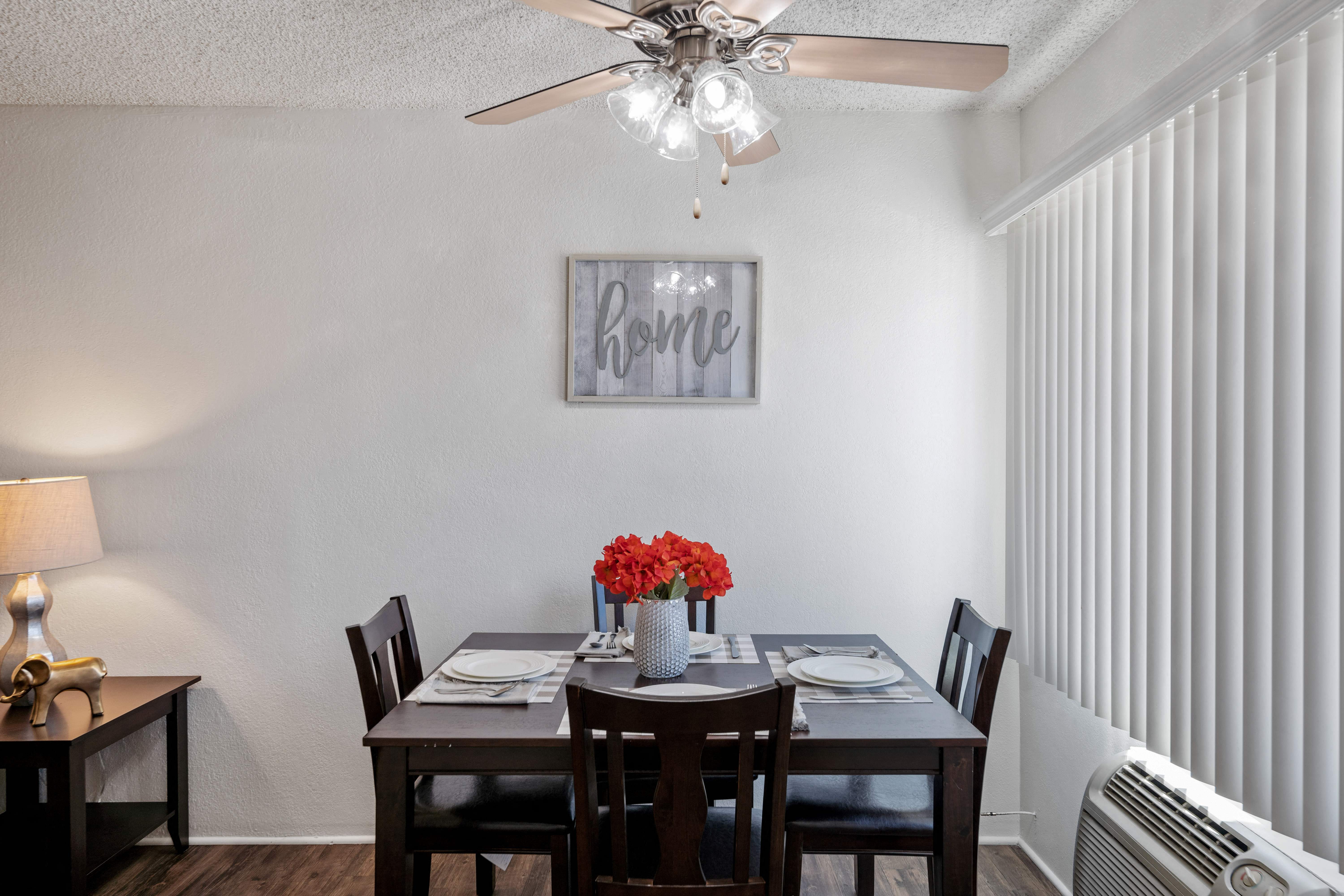 A dining room with a table set for four and a fan on the ceiling.