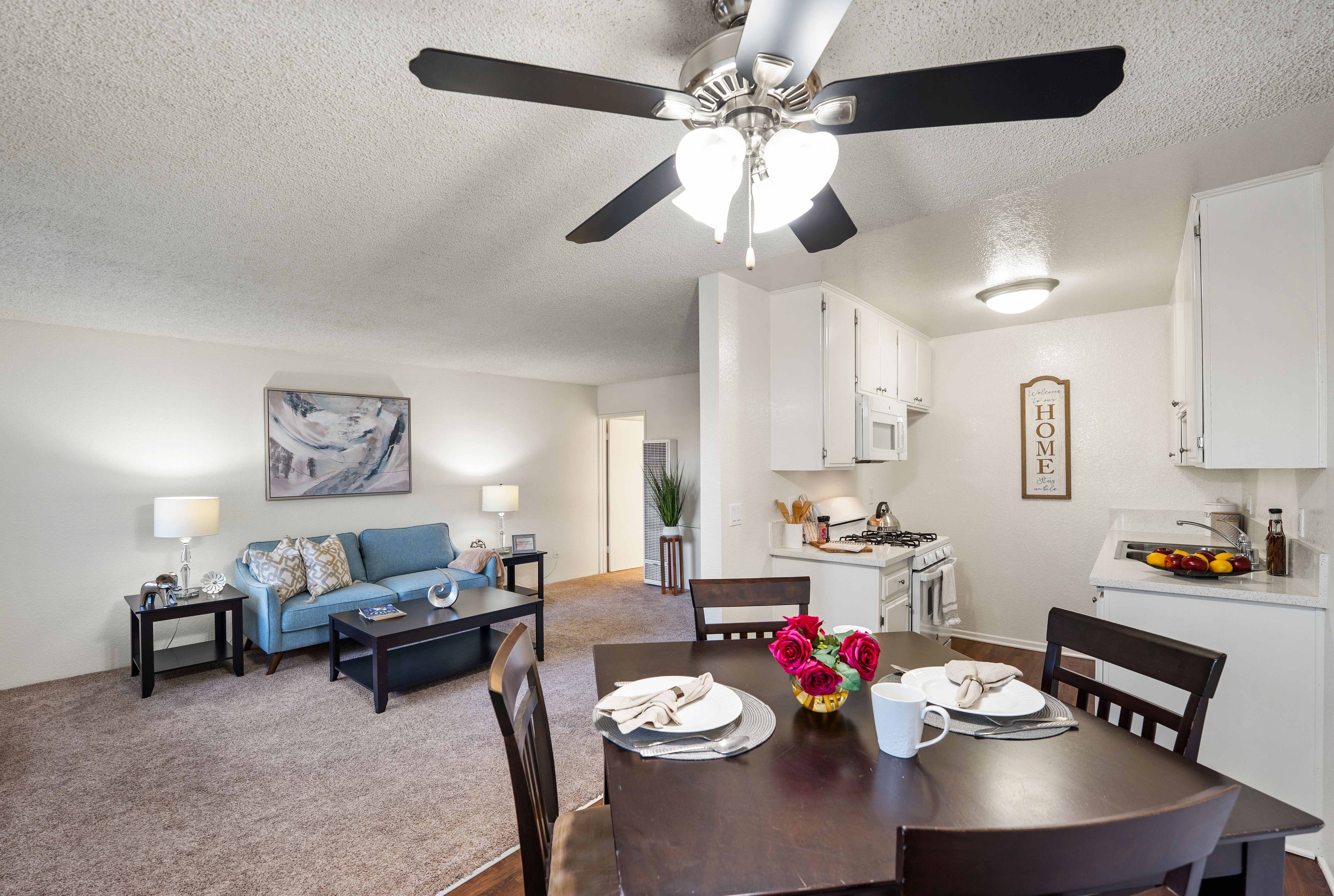 A dining room with a table set for two and a living room with a couch and lamp in the background.