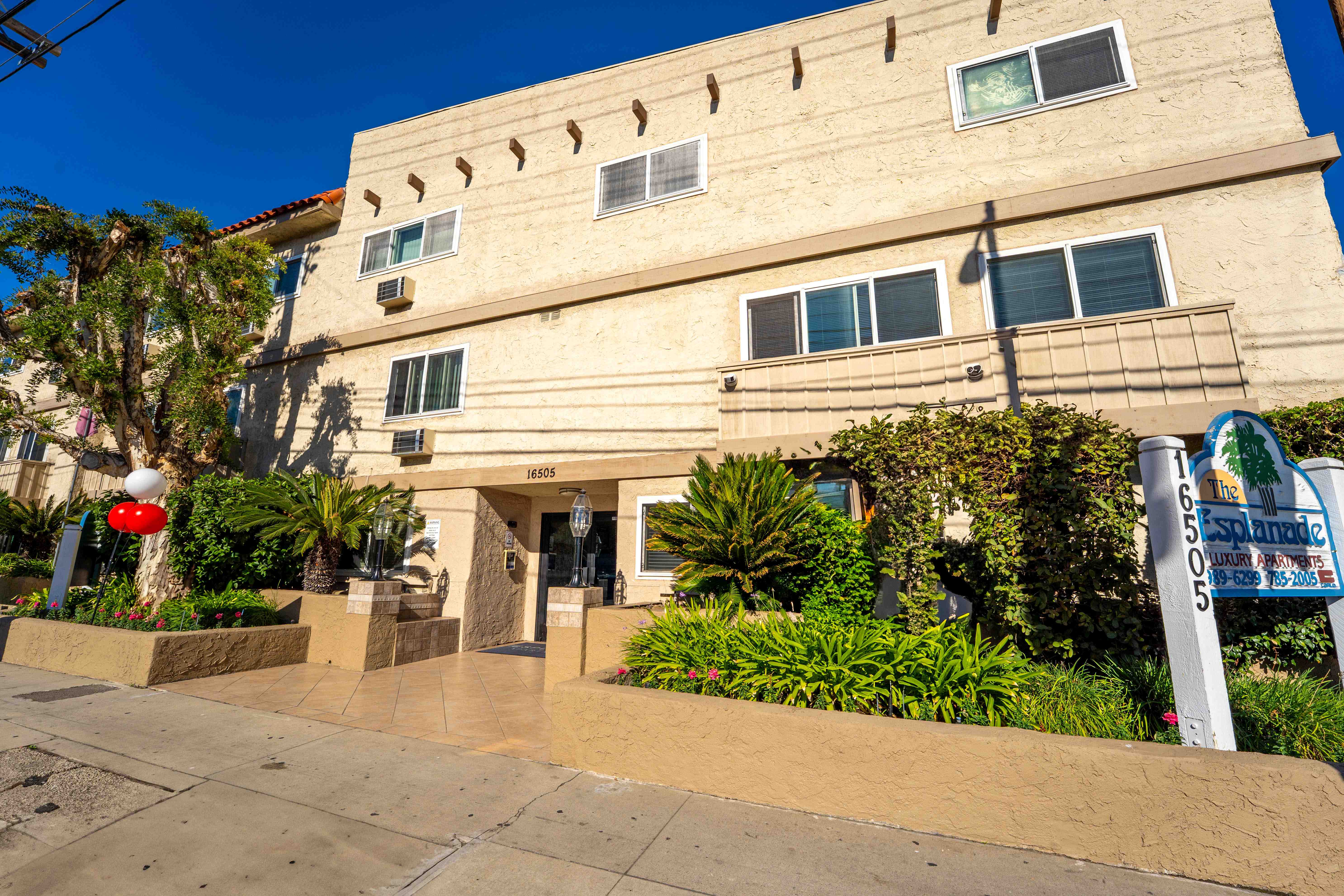 The exterior of The Esplanade with lush landscaping, a tiled entryway, and a prominent property sign.