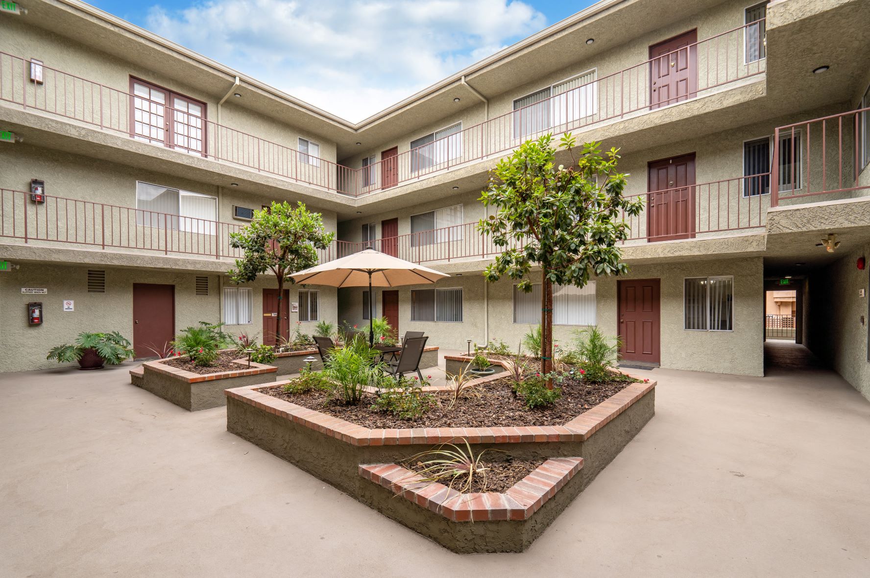 Beautifully manicured courtyard at the Hallmark Apartments in Studio City, showcasing the trees, a sitting area, and in the background are the apartment homes and the leasing office.