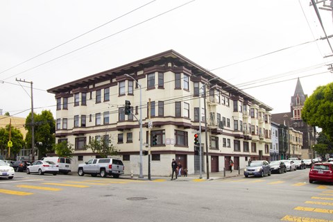 A street view of a multi-story building with cars parked in front.
