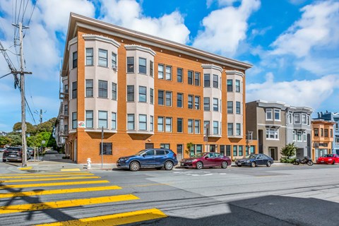 A street view of a multi-story building with cars parked in front.