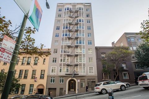 A tall building with a grey facade stands in front of a tree.