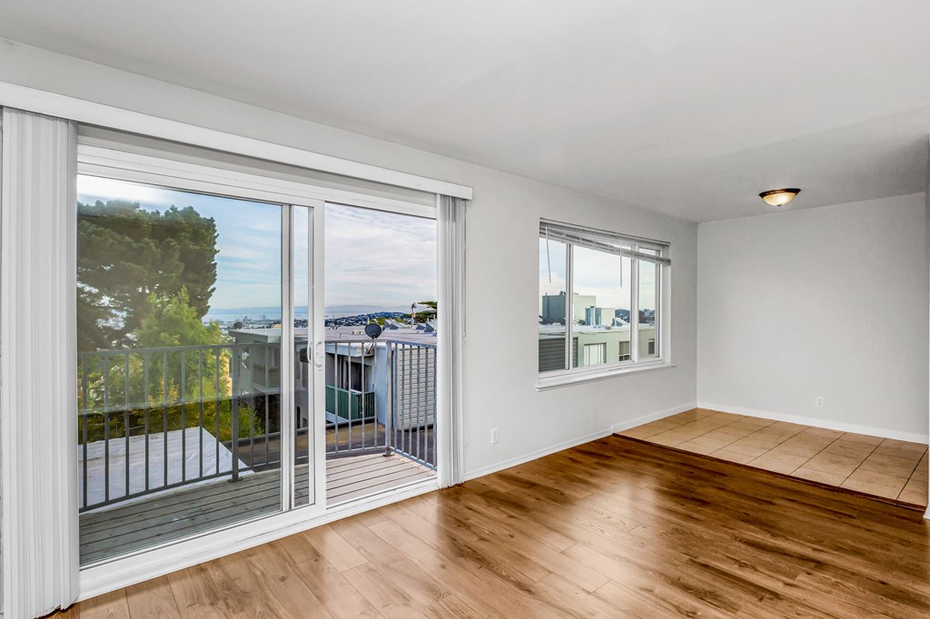 A room with wooden floors and a view of the outside through the windows.