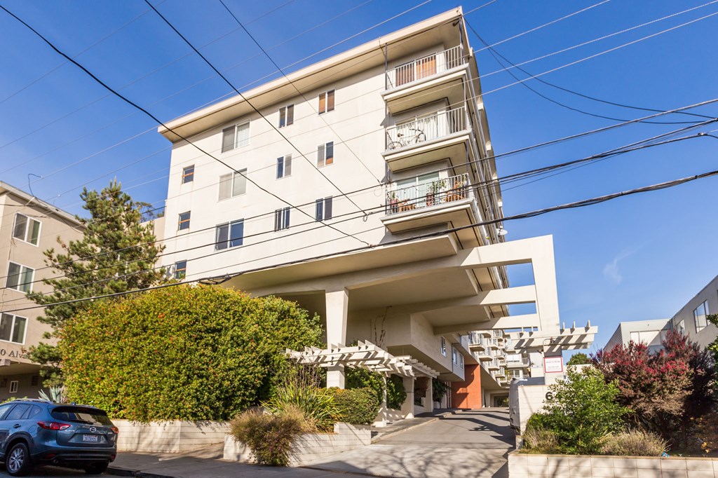 A modern white apartment building with balconies and a car parked in front.
