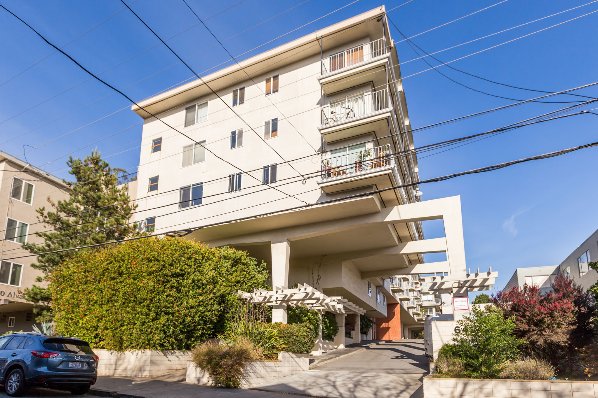 A modern white apartment building with a car parked in front.