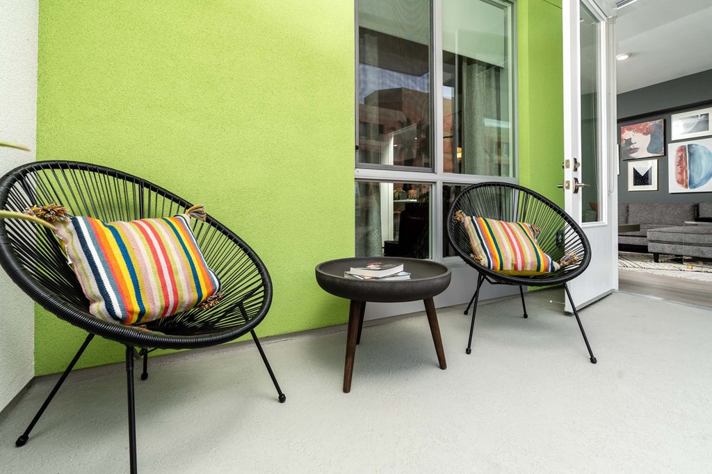 two chairs and a coffee table on a porch with a green wall