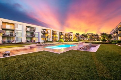 a rendering of an apartment complex with a pool and a sunset in the sky
